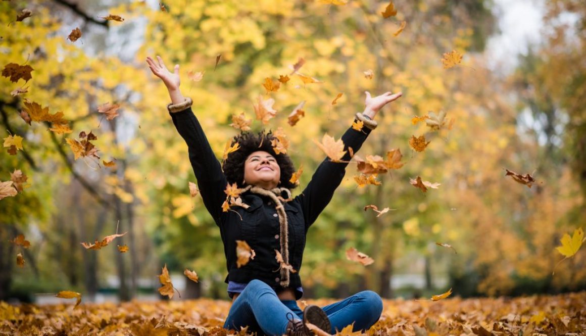 Joyous teen playing with dry maple leaves